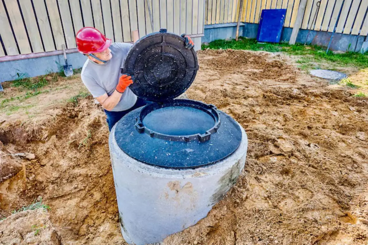Worker lifting the lid off a concrete septic tank access riser in a yard