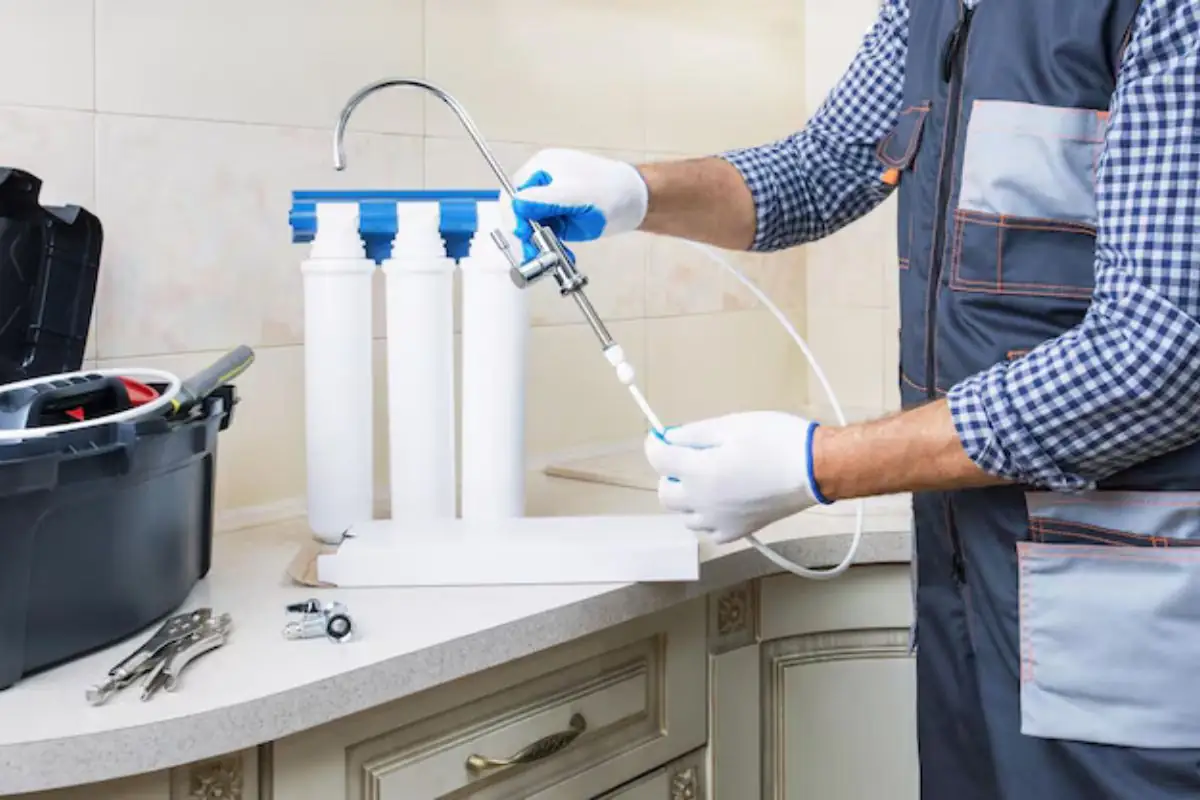 Technician installing a three-stage water filter system at a kitchen counter